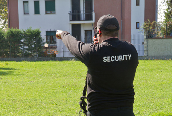 Zu sehen ist eine uniformierte Sicherheitskraft mit einem Funkgerät auf weitläufigem Gelände.